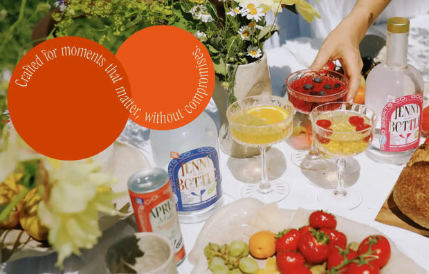 Przezroczysta szklana butelka z złotą zakrętką i różową etykietą z nazwą marki ’jenny bottle’.